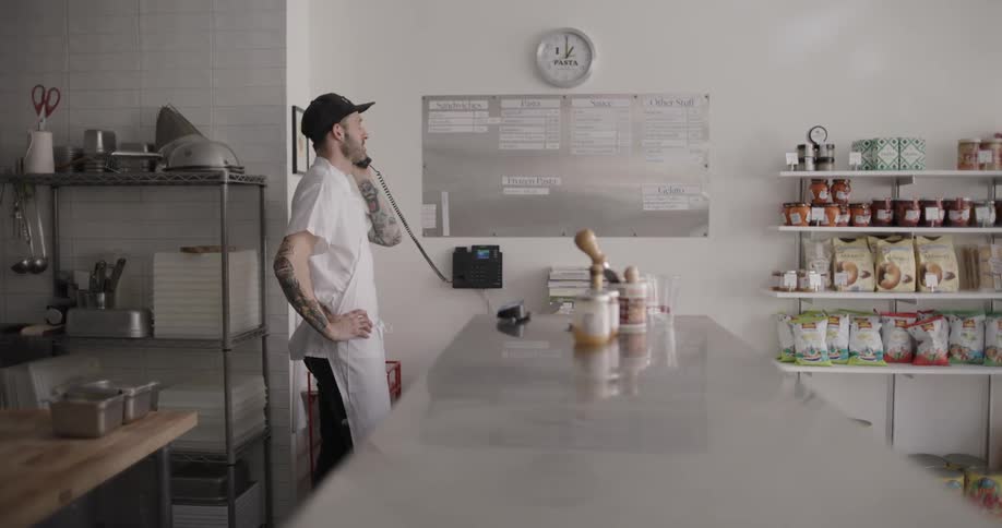 Man in a white coat inside an establishment talking on the corded phone