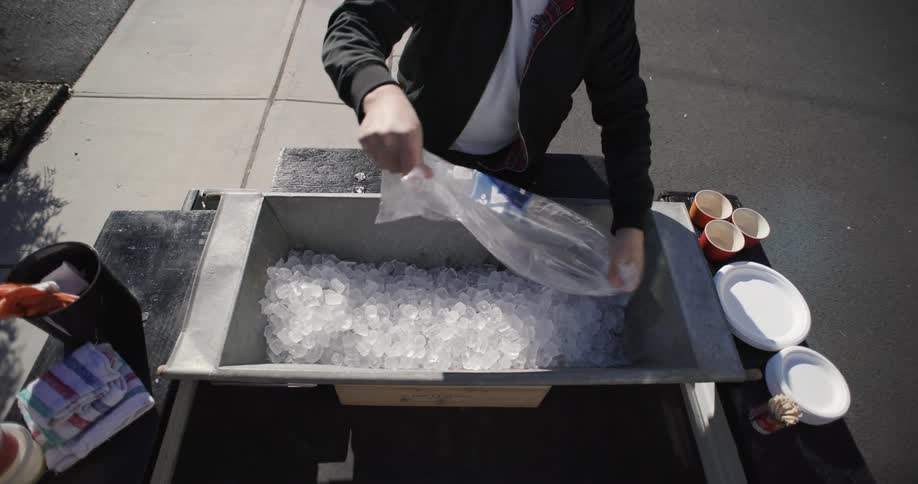 A person pouring ice from a plastic container into an empty tank