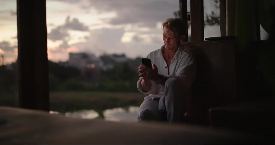Man sitting in the patio at sunset looks at his phone