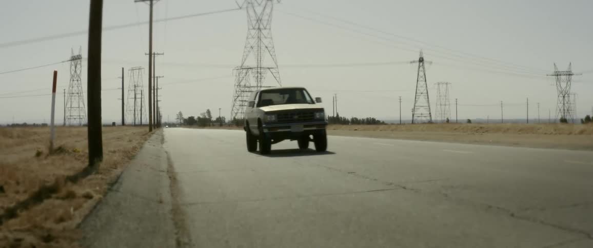 Old bronco drives by on a country road with large utility line towers in the background