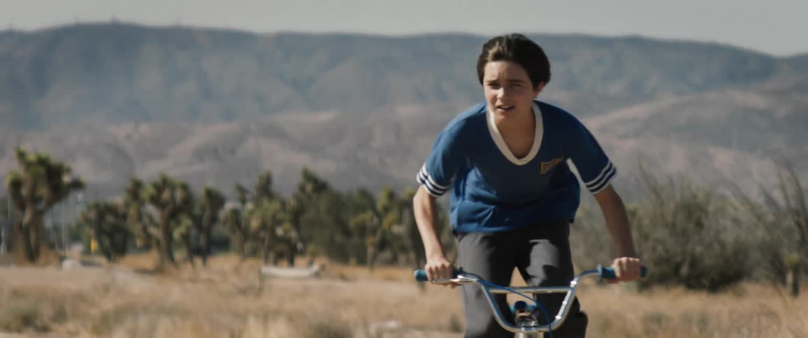Young boy riding a bicycle in a place with greenery and mountains