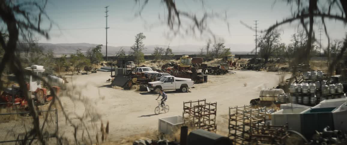 A person driving a bicycle through a junkyard under a clear sky