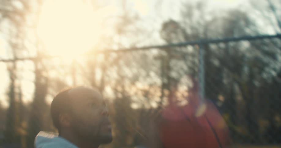 Man wearing a gray hoodie plays basketball at sunset