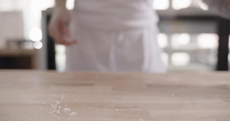 A cook removes a dessert plate from a table then cleans the surface with a cloth