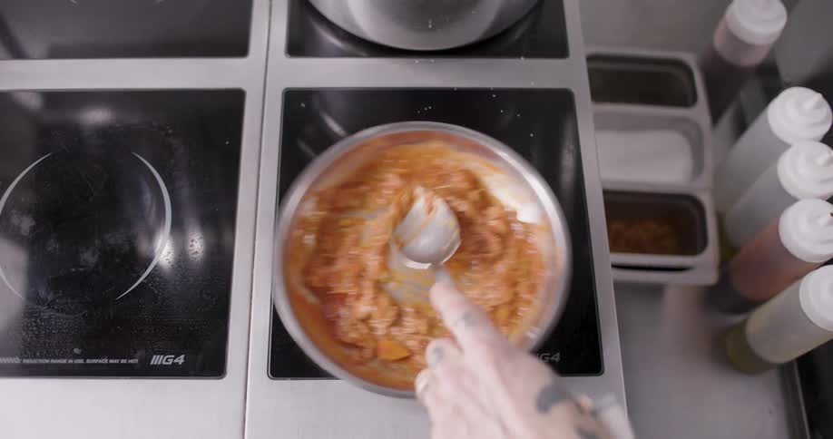 A person is preparing food in a pan and is stirring it with a spoon on a stove with a black surface