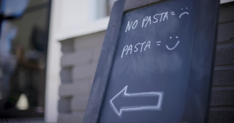 A small blackboard sign outside of a building advertises a businesss pasta