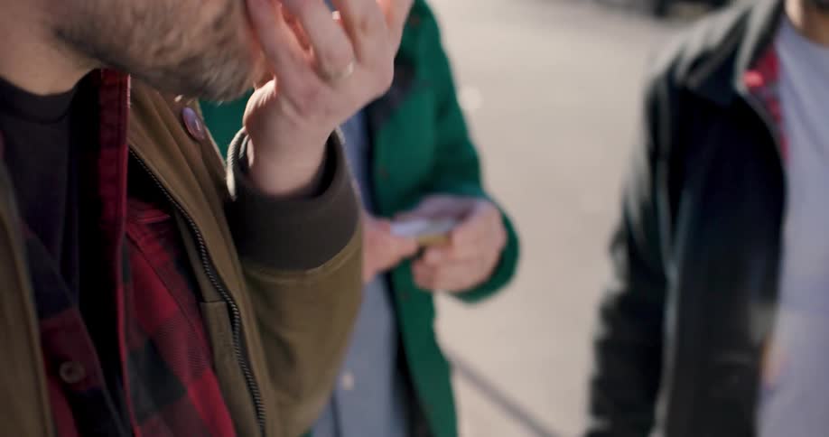 A man in the street opens an oyster taken from an ice box and serves it to another man who eats and enjoys it while another looks on