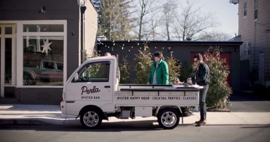 An oyster vendor serves two customers on a small truck in the streets