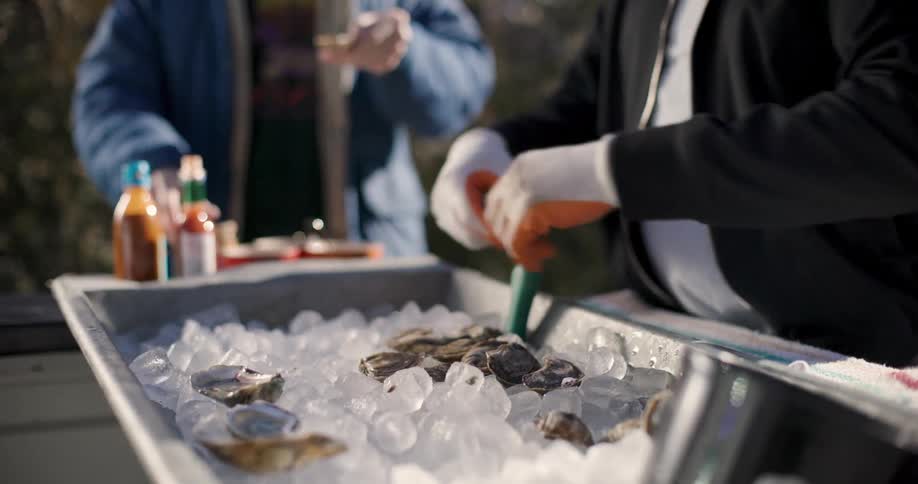 Hands of a man with gloves serving oysters in a food truck to a customer