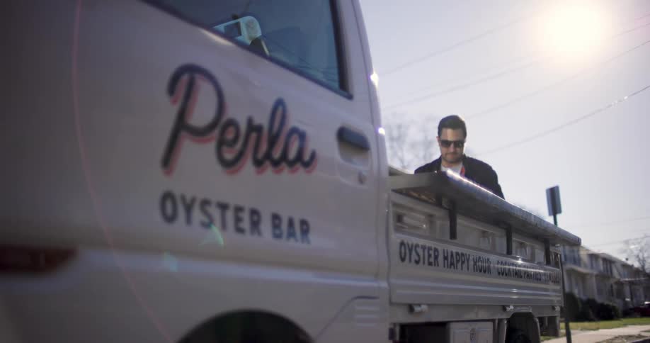 Caterer stands near back of food services truck parked in residential neighborhood on a sunny day