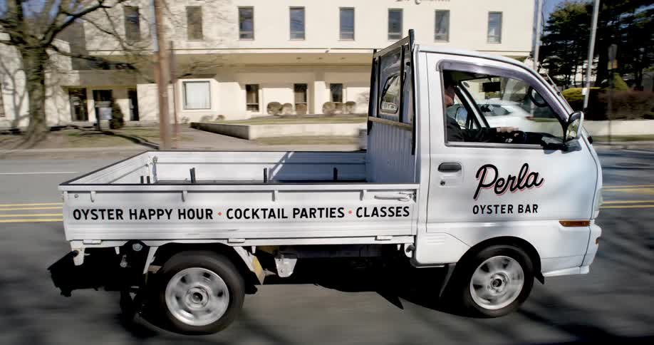 A man driving a small truck through the streets of a neighborhood
