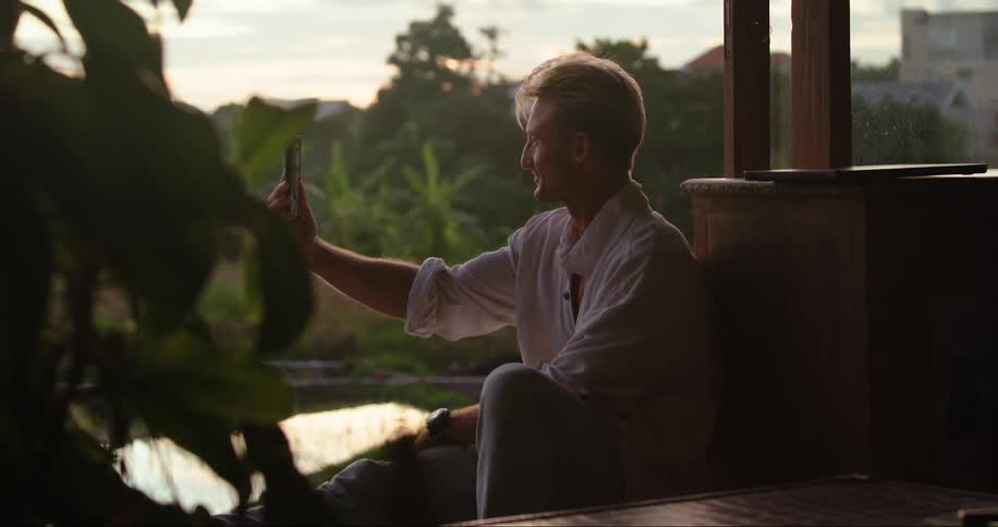 A man having a video call on a phone on the patio at sunset