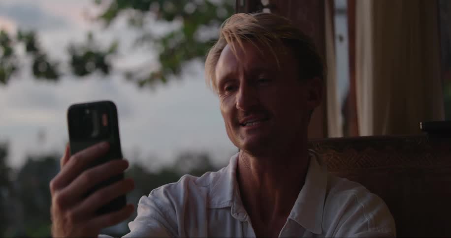 Blonde man wearing a white polo shirt makes video call on smartphone
