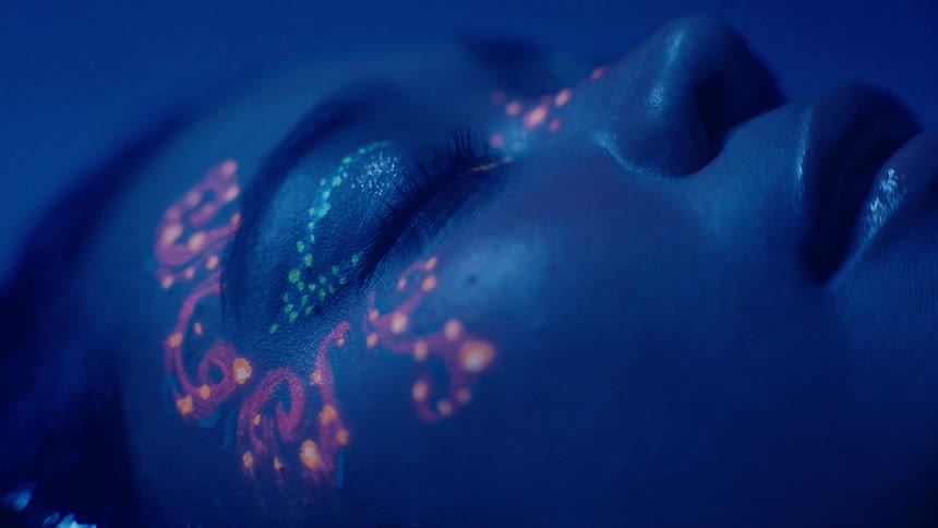 A woman has her eyes closed and her head is in the water and she has pink paint on her face