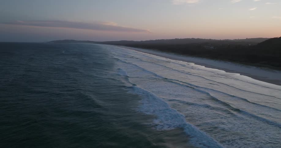 Aerial of ocean waves breaking against the beach at sunset