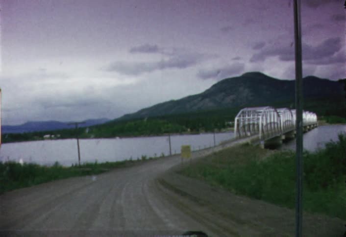 A vehicle travels down a road approaching a bridge over a body of water