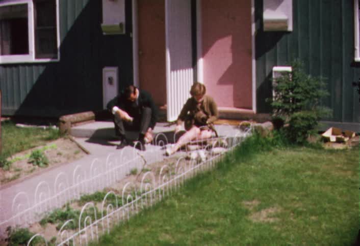 A man sits outside as a woman tosses kittens into an enclosure