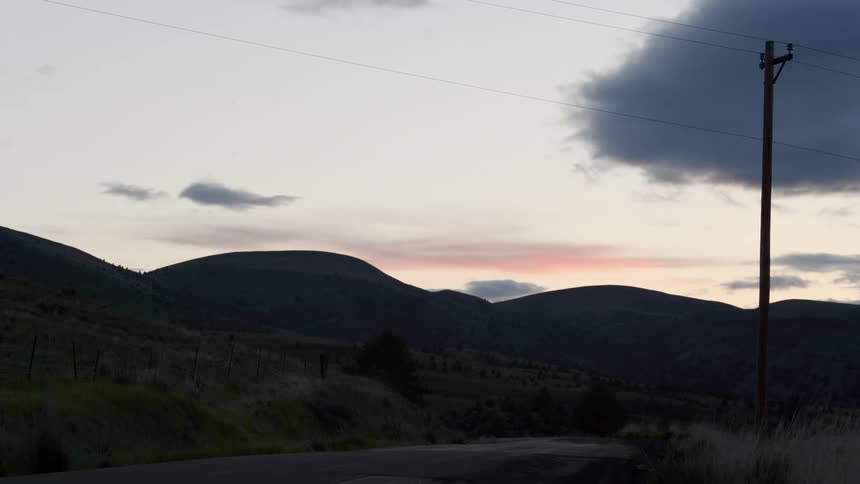 Red and dark clouds pass over hills bordering country road