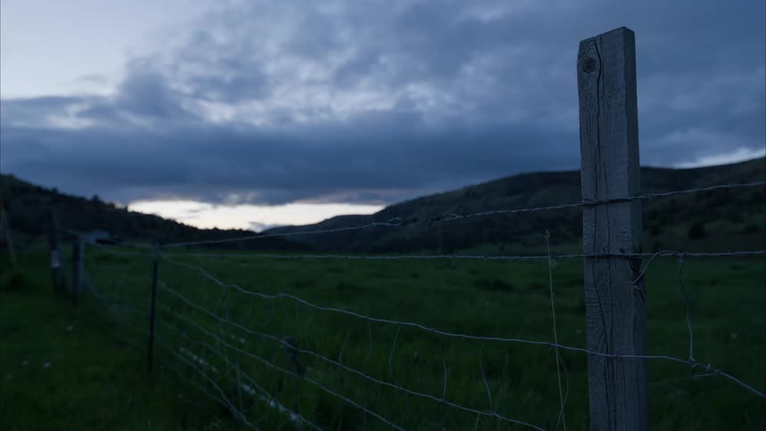 Barbed wire fence in a rural area with mountains on the horizon on a morning