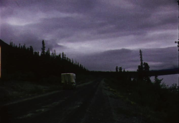 A cab-over camper drives down a road under stormy skies