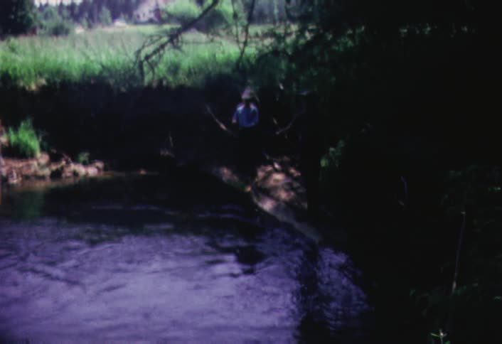 Two people standing on the bank of a small river