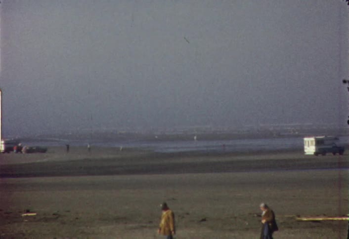 Groups of people walk on a beach where campers are parked