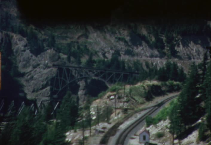 A vehicle travels on a mountain road with railroad tracks below