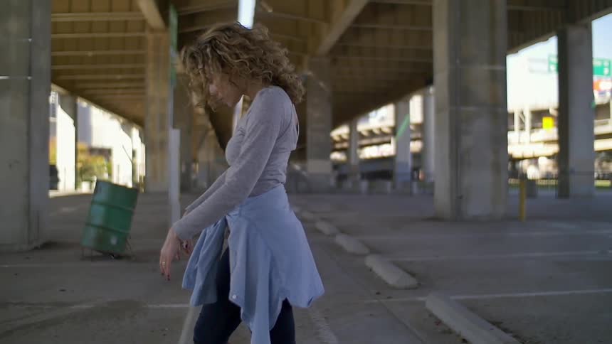 Woman outside dancing under a bridge