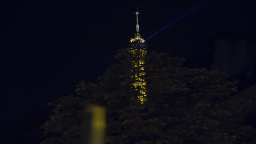 The eiffel tower shining a spotlight at night