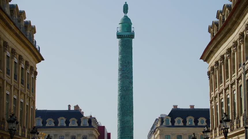A large pillar with a statue at the top stands near apartment buildings