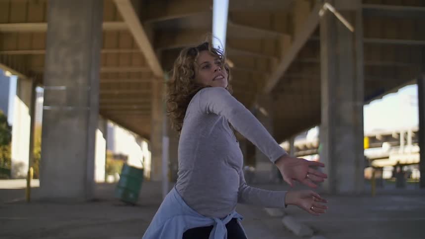 A woman is dancing under an over-pass on a sunny day
