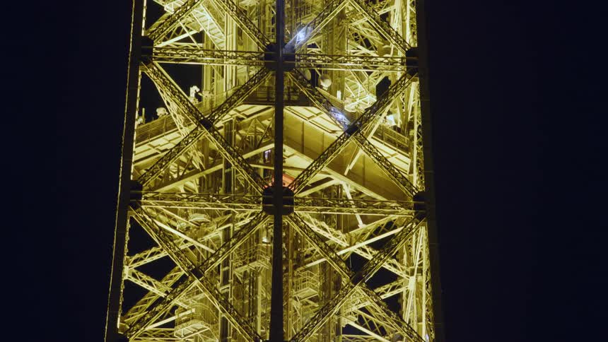 An elevator in the eiffel tower going up and the tower is all lit up yellow and shining