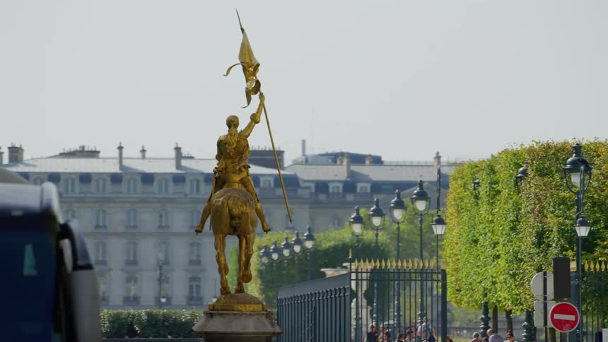 A golden statue in front of a fenced city garden