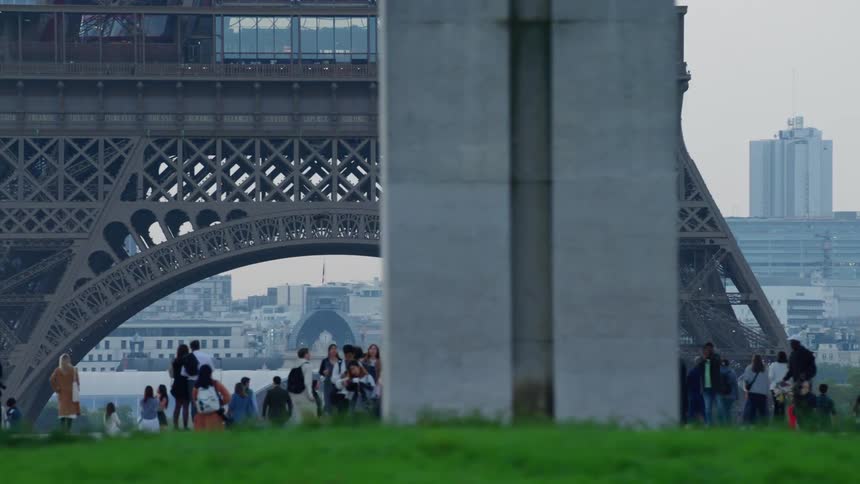 The eiffel tower seen by many tourists who are in front admiring it and taking photos and there is a sign saying welcome to paris