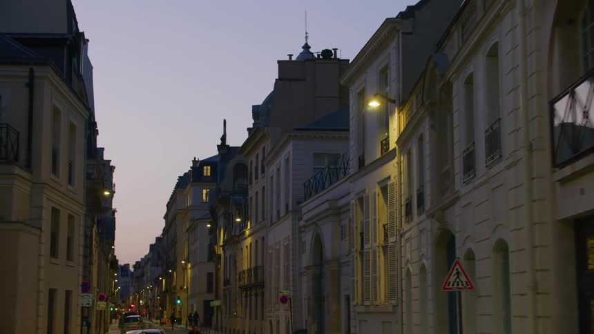 People move along narrow road near parked cars at night