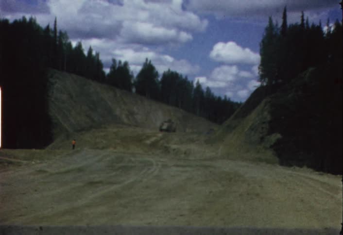 A vehicle drives on a dirt path surrounded by trees
