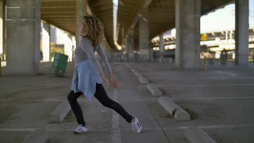A woman is dancing under an overpass on a sunny day
