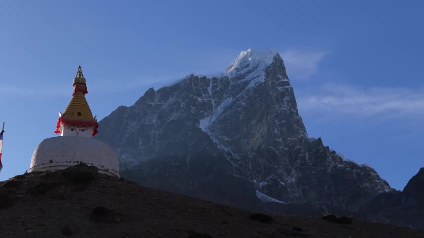 Mountain with snowy peak towers over structure with pointed top and drawn eyes