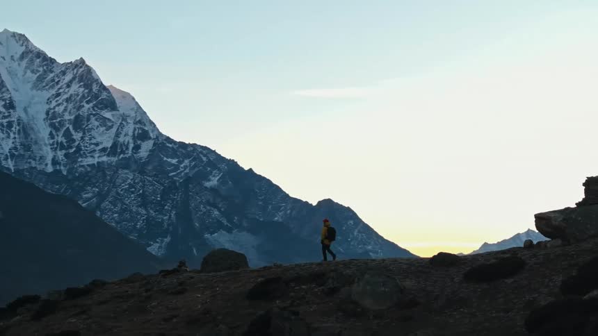 A lone hiker walks across a mountain ridge above a scenic landscape