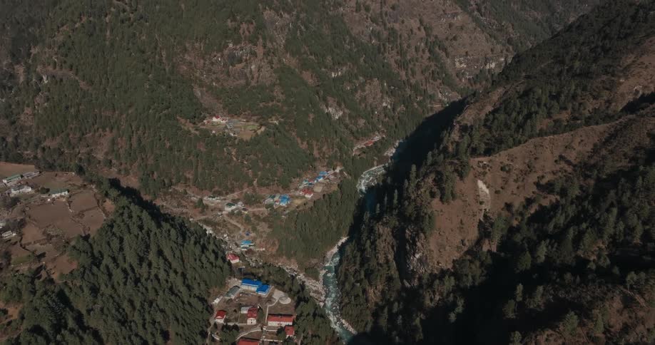 Red and white roofed buildings sit on plateau and in valley among forested mountains