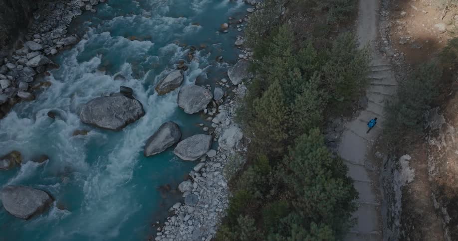 An aerial view of a person walking along the bank of a flowing river