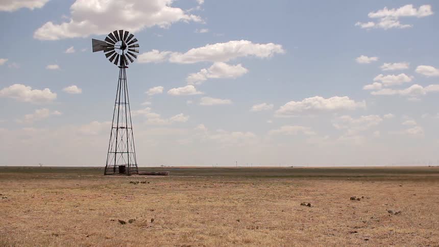 A windmill turns slowly in an open field