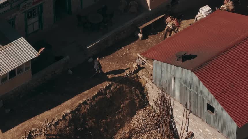 Aerial of a man walking behind horses on a path between houses at midday