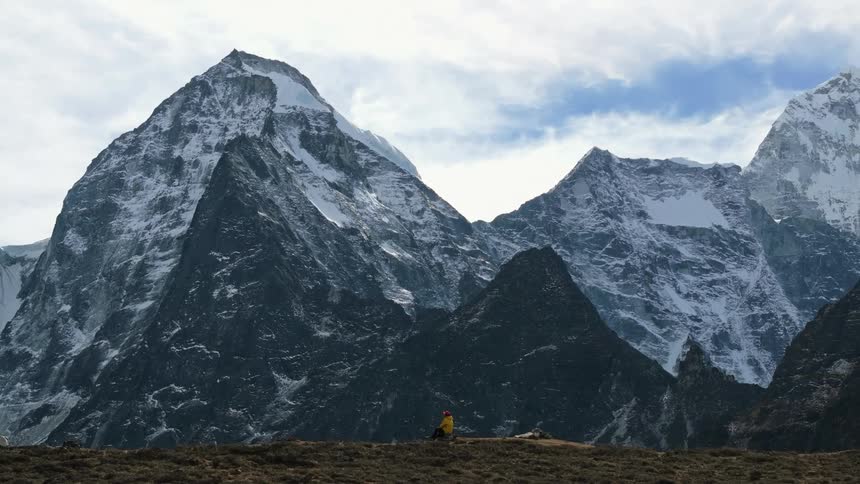 A man sit on a mountain while opening his backpack at daytime