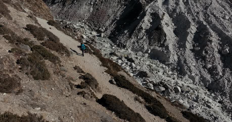 Backpacker hikes along hill across valley from gray mountain slope