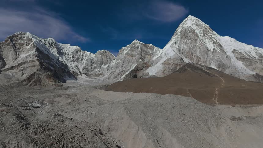 A region with the ground covered in gravel and there is a huge mountain with snow on top
