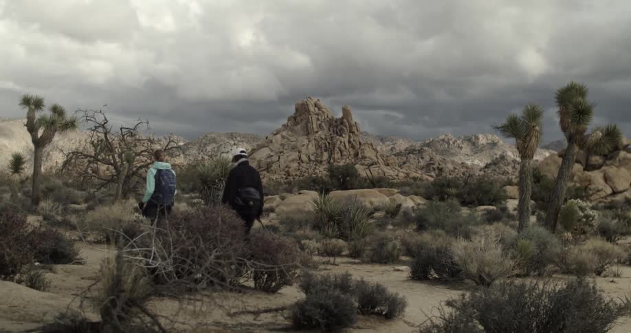 Two people are hiking in a desert location beneath storm clouds