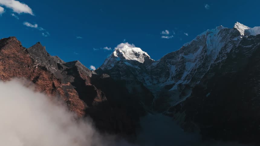Landscape of mountain ranges with their peaks covered by snow on a blue sky day with few clouds