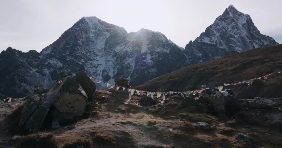 Colorful pendants flutter on rope strung on ridge across valley from mountains on a cloudy day