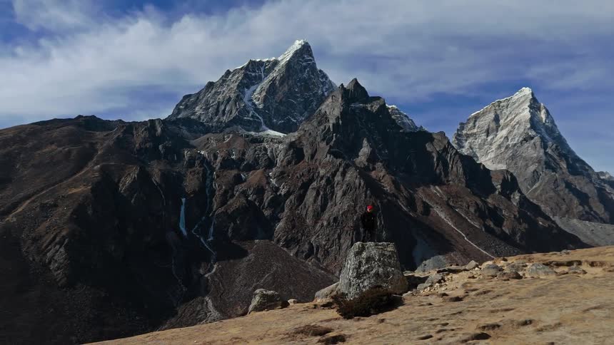 A man on top of a rock admiring the landscape with a frozen river in the mountains